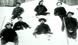 Seven men wearing coats and hats, sitting and standing in a pile of snow, facing the camera