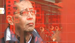 Closeup of a man wearing glasses, looking pensively off-screen, with superimposed photo of red vertical signs with Chinese words and building reflections.
