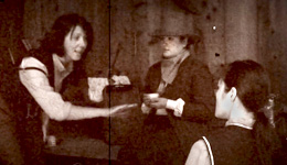 Sepia-toned scene of three people facing one another. One leaning over another, arm gesturing in an emphatic swipe.